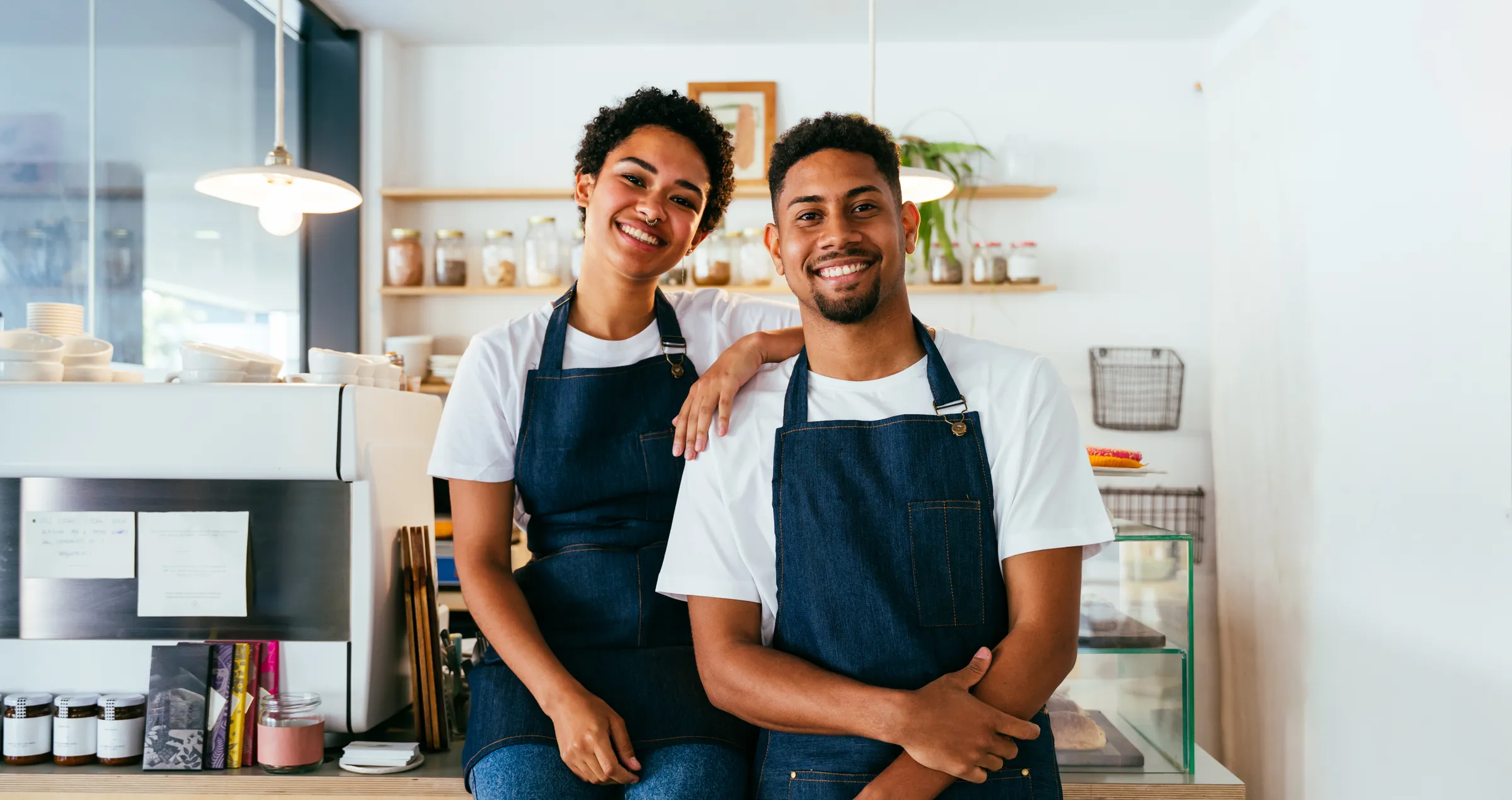 Two smiling café owners in aprons behind their counter